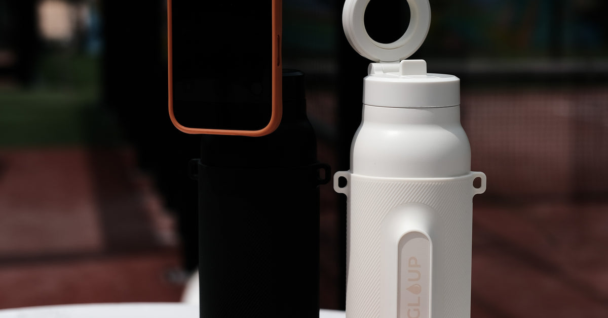 Gloup Grip flessen in Cream, Pink en Black met telefoon op een tafel bij de padelbaan
