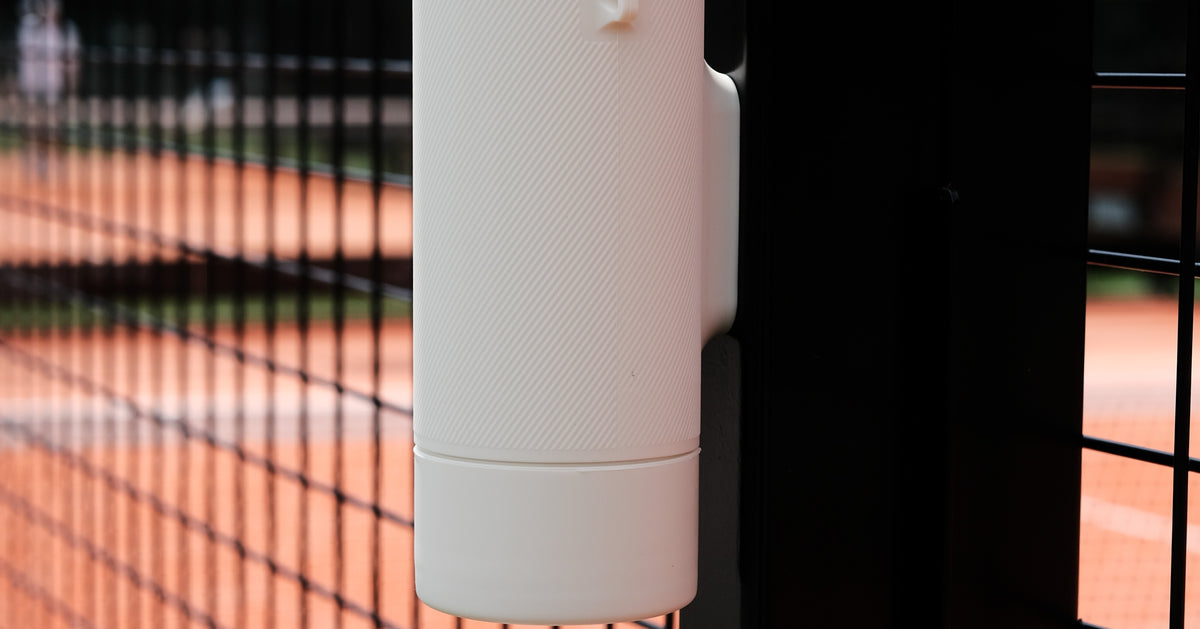 Gloup Grip fles magnetisch bevestigd aan het hek van een padelbaan